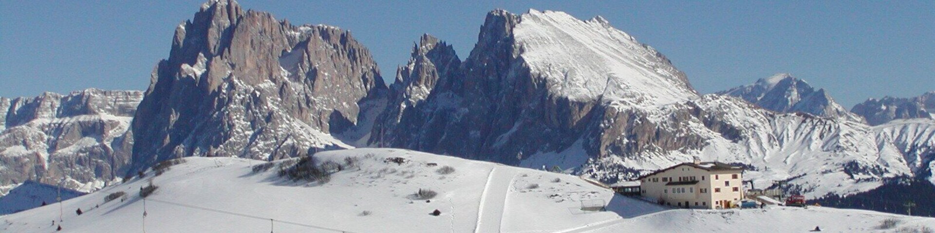 Pista de esquí nevada con montañas al fondo, un telesilla y una cabaña.