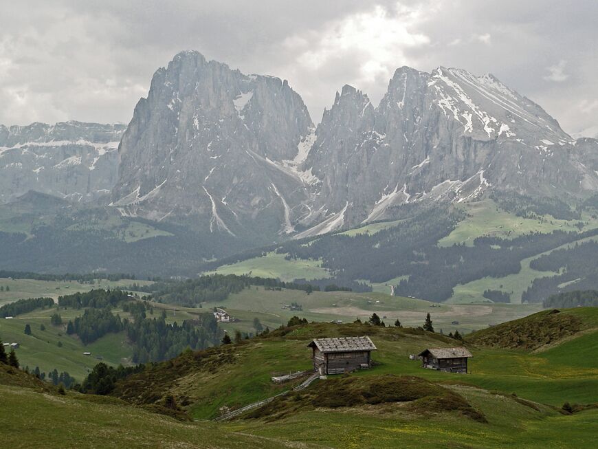 Un paisaje montañoso con dos picos destacados, valles verdes y pequeños edificios.