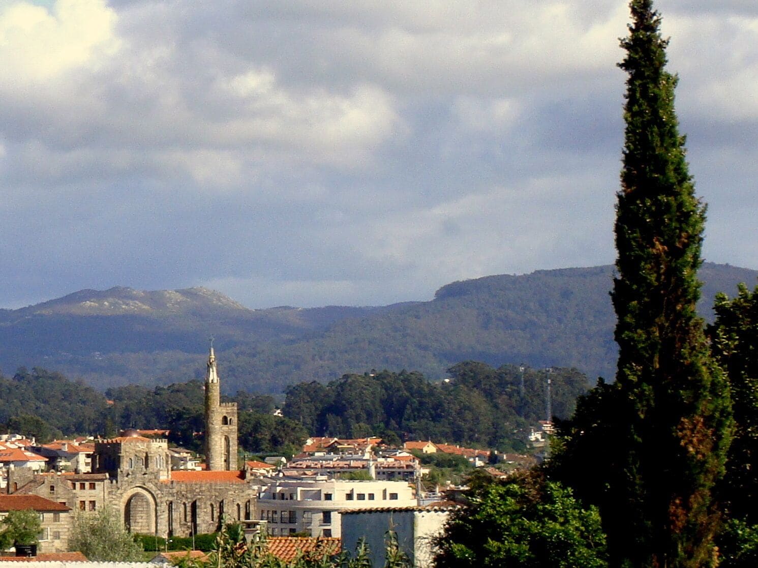 Un pueblo con una torre de iglesia destacada, rodeado de edificios y montañas al fondo.