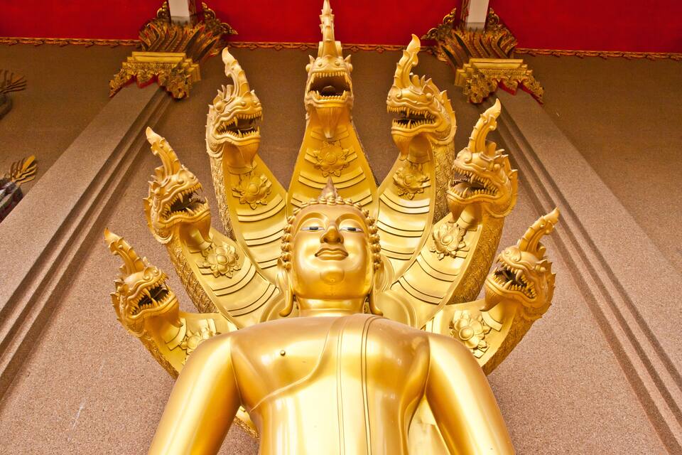 En gyllene Buddha-staty i liggande ställning, omgiven av utsmyckade gyllene drakhuvuden.