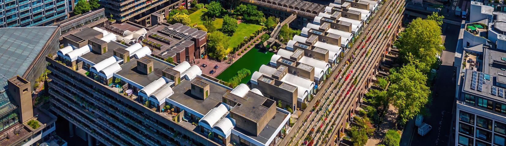 Colorful aerial view of London's Barbican Estate with high-rise buildings, modern architecture, and city skyline under a blue sky