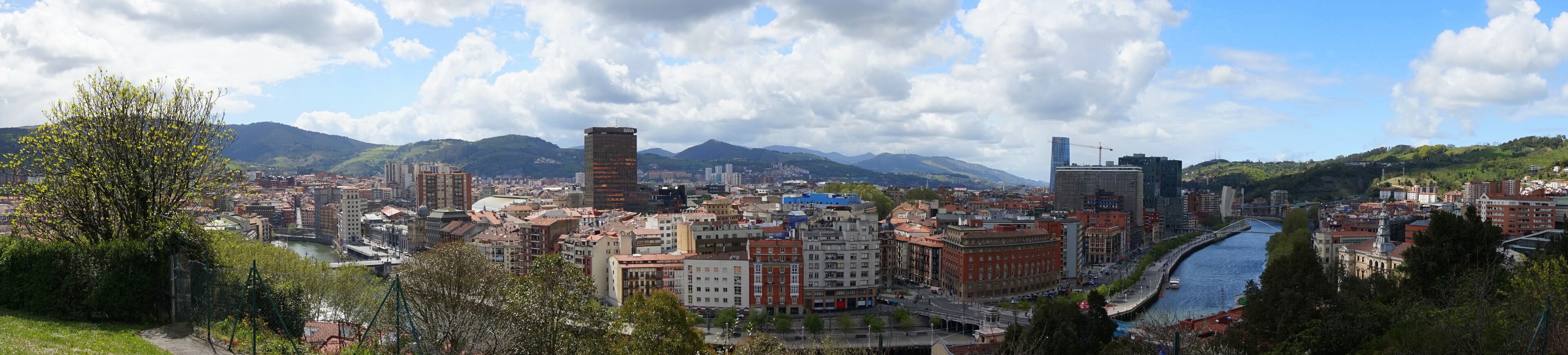 A cityscape with a river, mountains, and a mix of modern and traditional architecture.