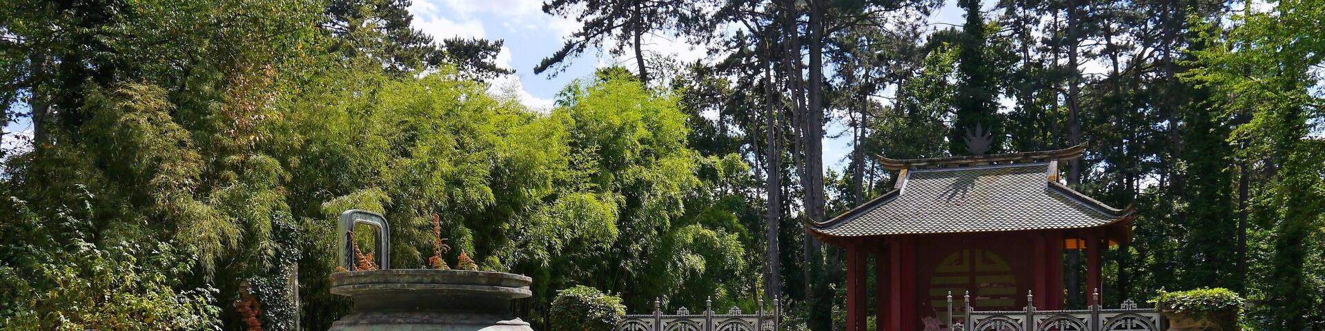 A traditional Japanese pagoda with a stone lantern and steps leading up to it, surrounded by lush greenery.