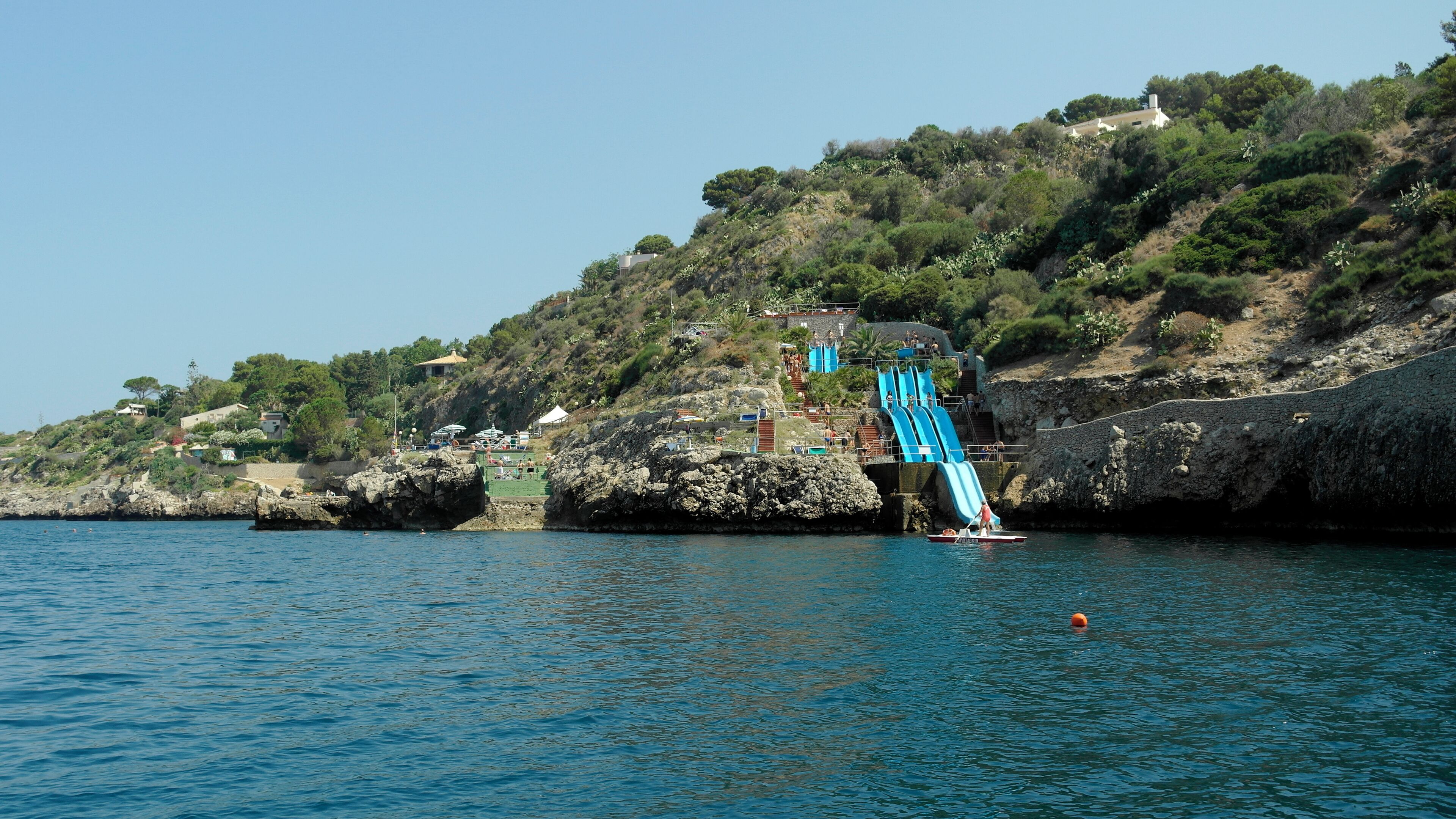 A coastal area with a rocky shoreline, a small boat, and a water slide extending into the sea.
