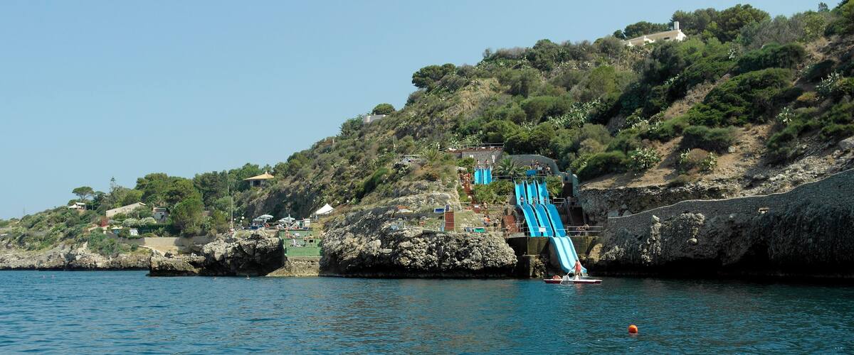 A coastal area with a rocky shoreline, a small boat, and a water slide extending into the sea.