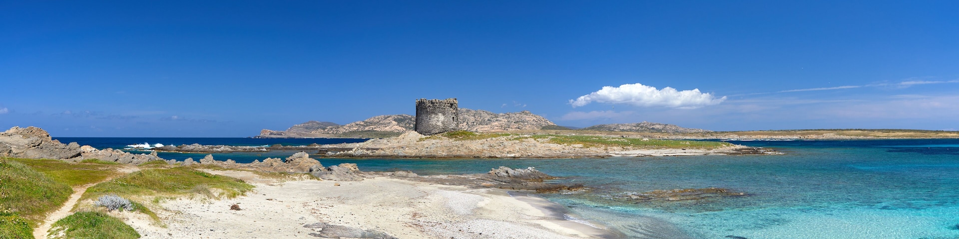 Un paisaje costero con un promontorio rocoso, aguas turquesas transparentes y una playa de arena.