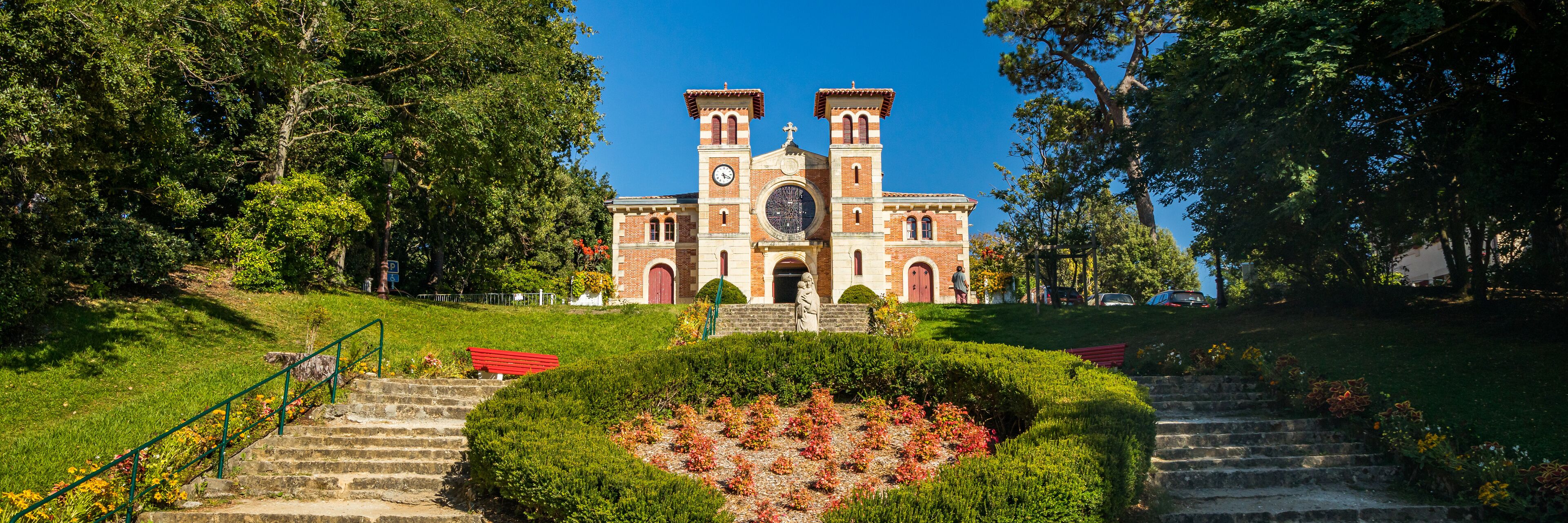 A historic church with twin towers, surrounded by lush greenery and stone steps leading up to it.