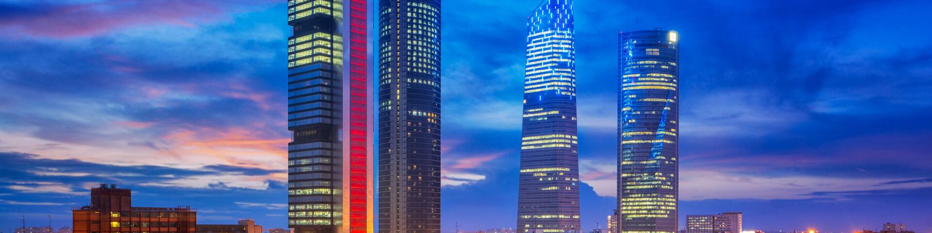A cityscape at dusk with illuminated skyscrapers and a busy highway.