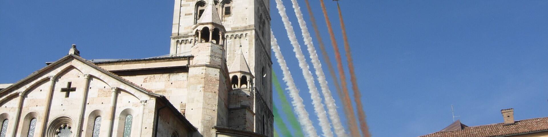 A historic church with a tall bell tower and a group of airplanes performing a flight formation with colored smoke trails.