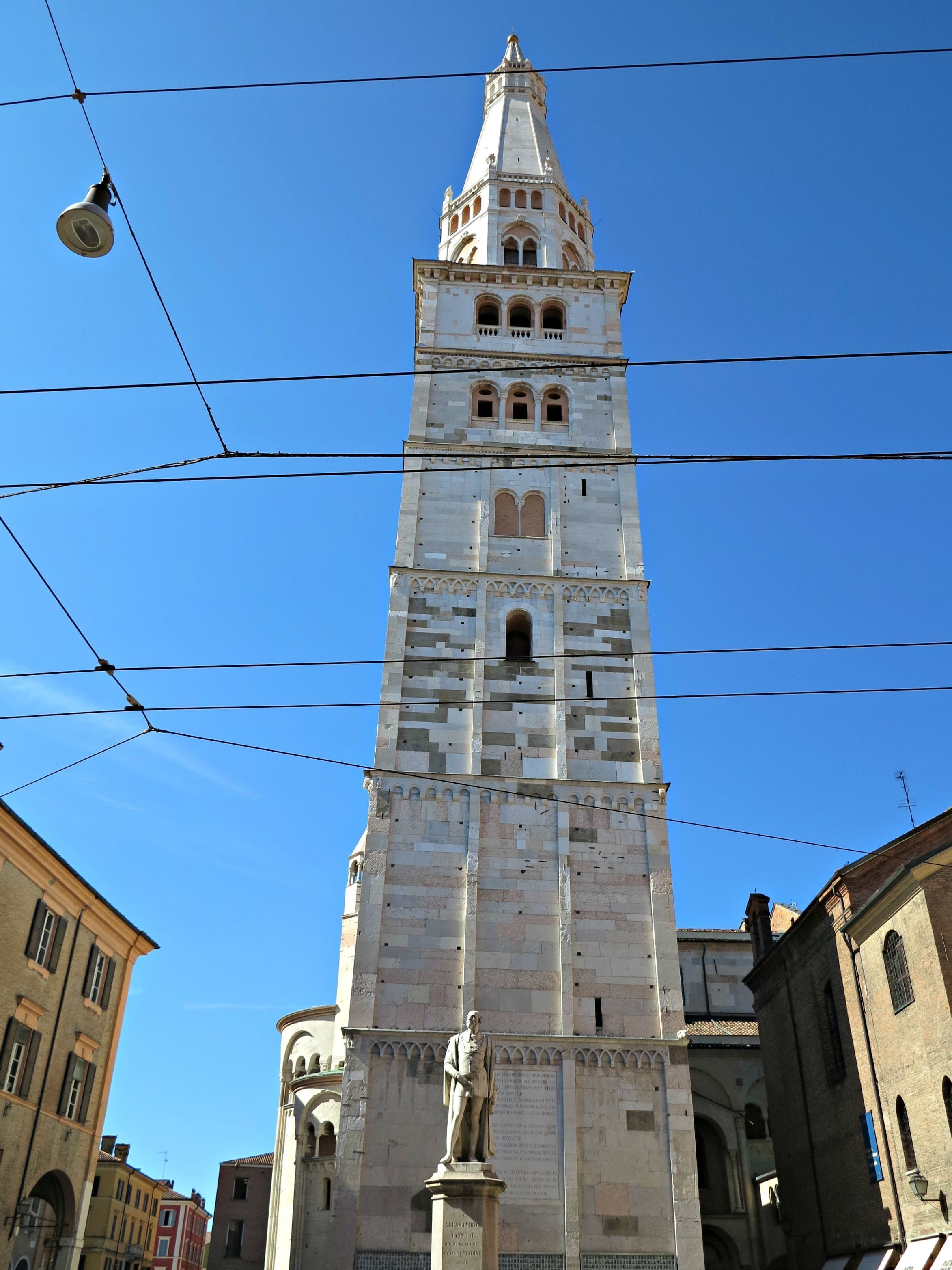 Ein hoher Turm mit einer Statue am Fuße, umgeben von Gebäuden.