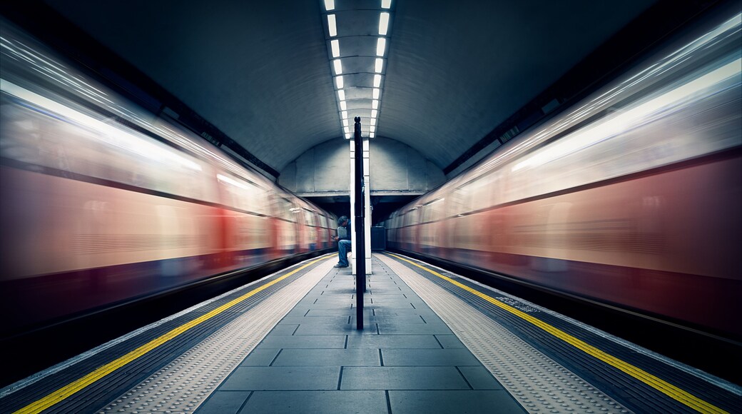 Two trains in motion and a seated commuter at London Tube Station, Clapham Common, Clapham, London