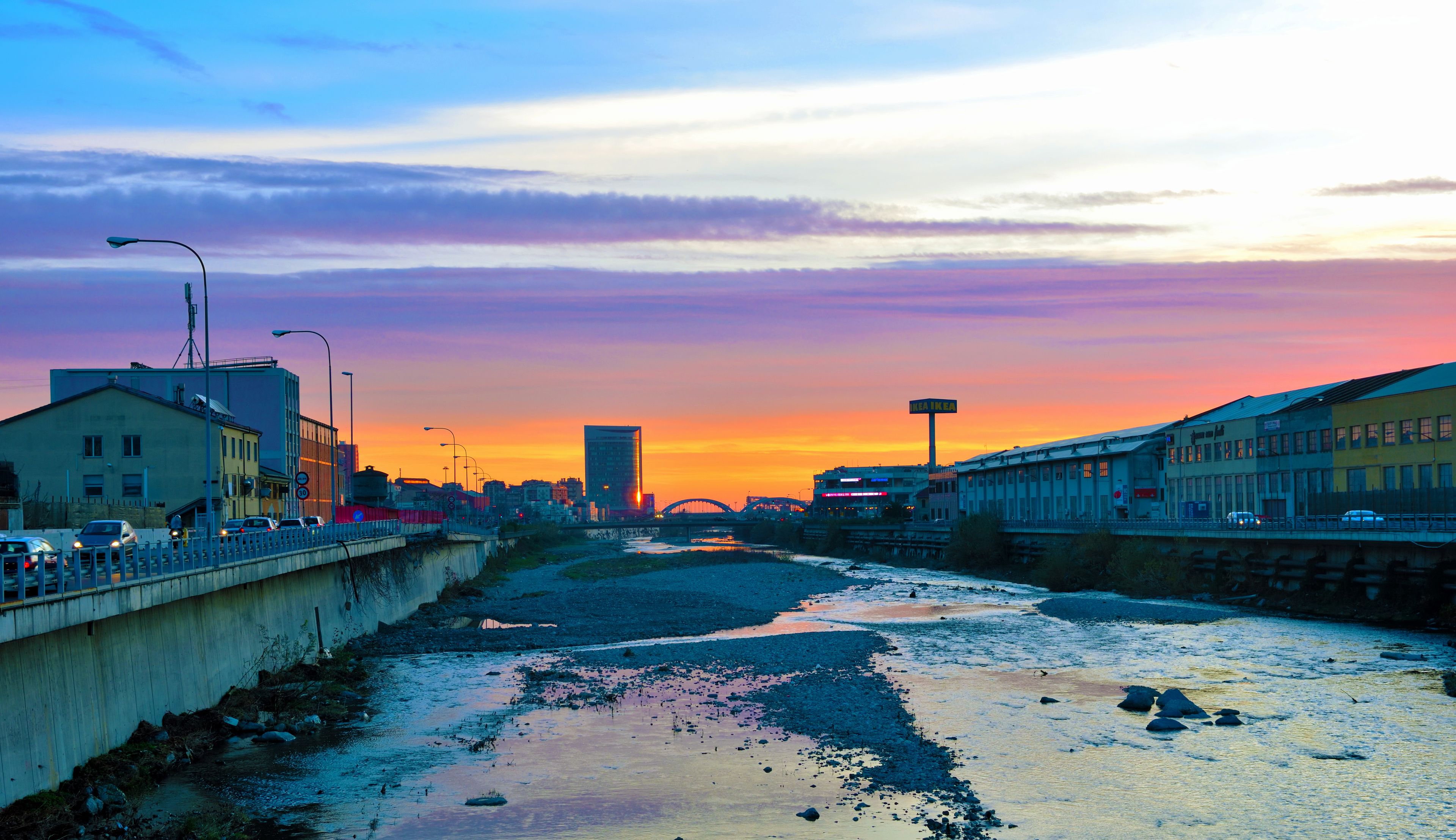 Ein Fluss im Abendrot mit einer Brücke, Gebäuden und einer Stadtansicht.