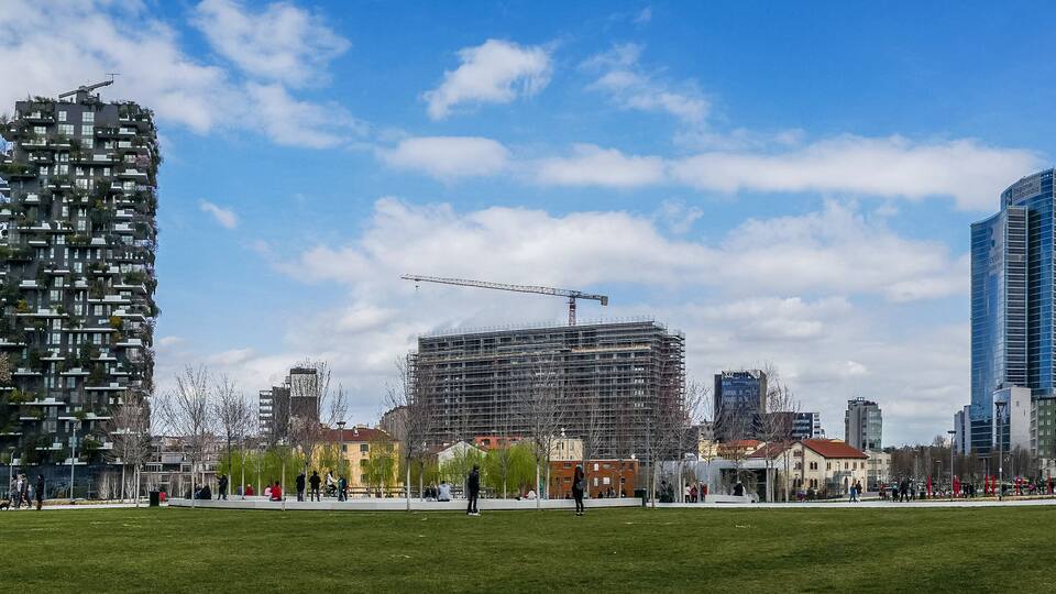 Eine Stadtansicht mit modernen Hochhäusern, einer Baustelle und einem Park mit Menschen.