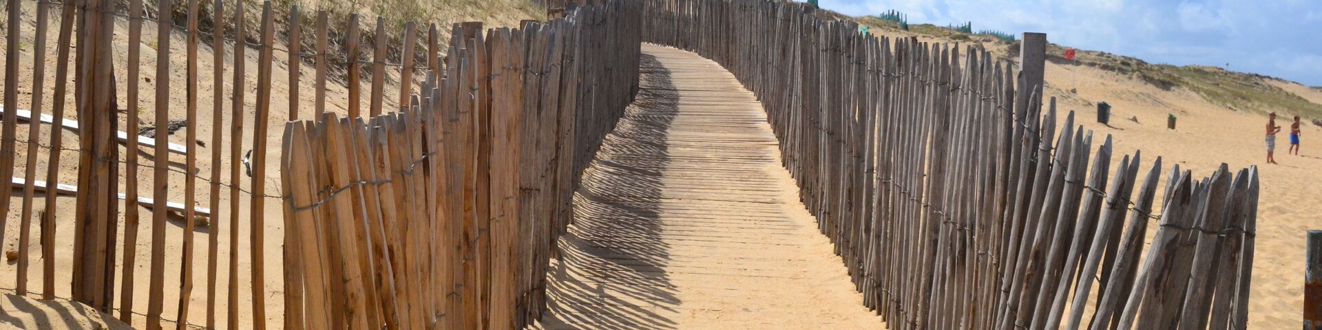 A wooden boardwalk leading up a sandy hill with a fence on either side.