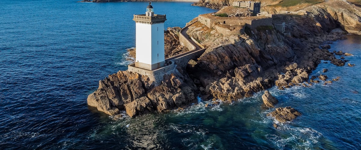 A lighthouse on a rocky coastline with clear blue waters.