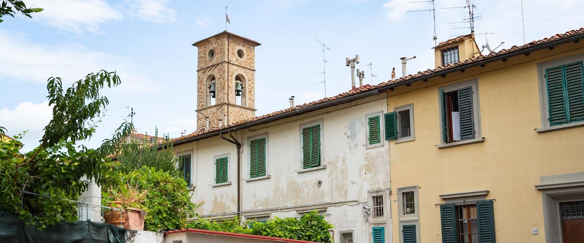 A street with a historic building, a bell tower, and a covered motorcycle.