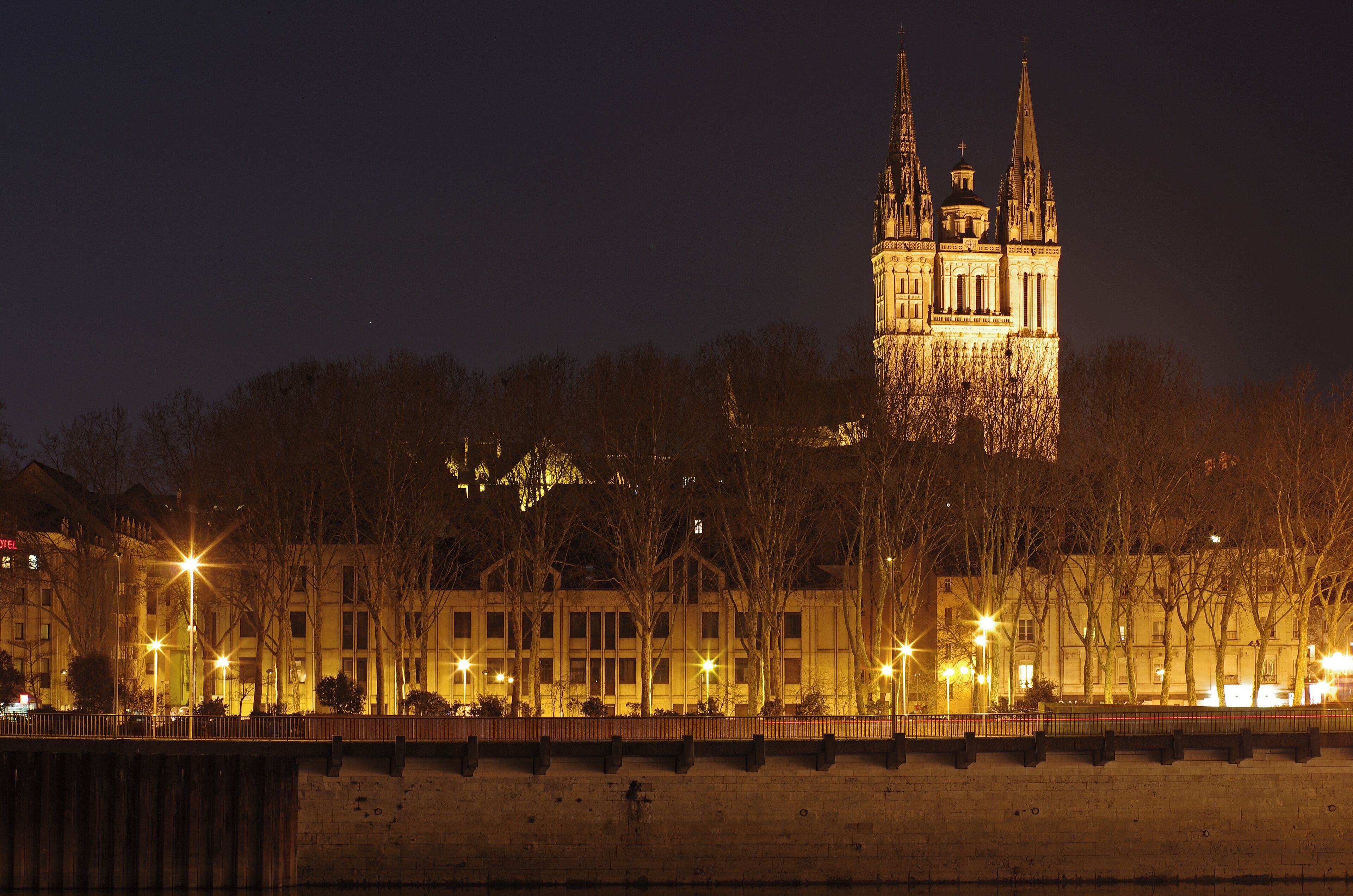 A lit-up cathedral with two spires, surrounded by trees and buildings.