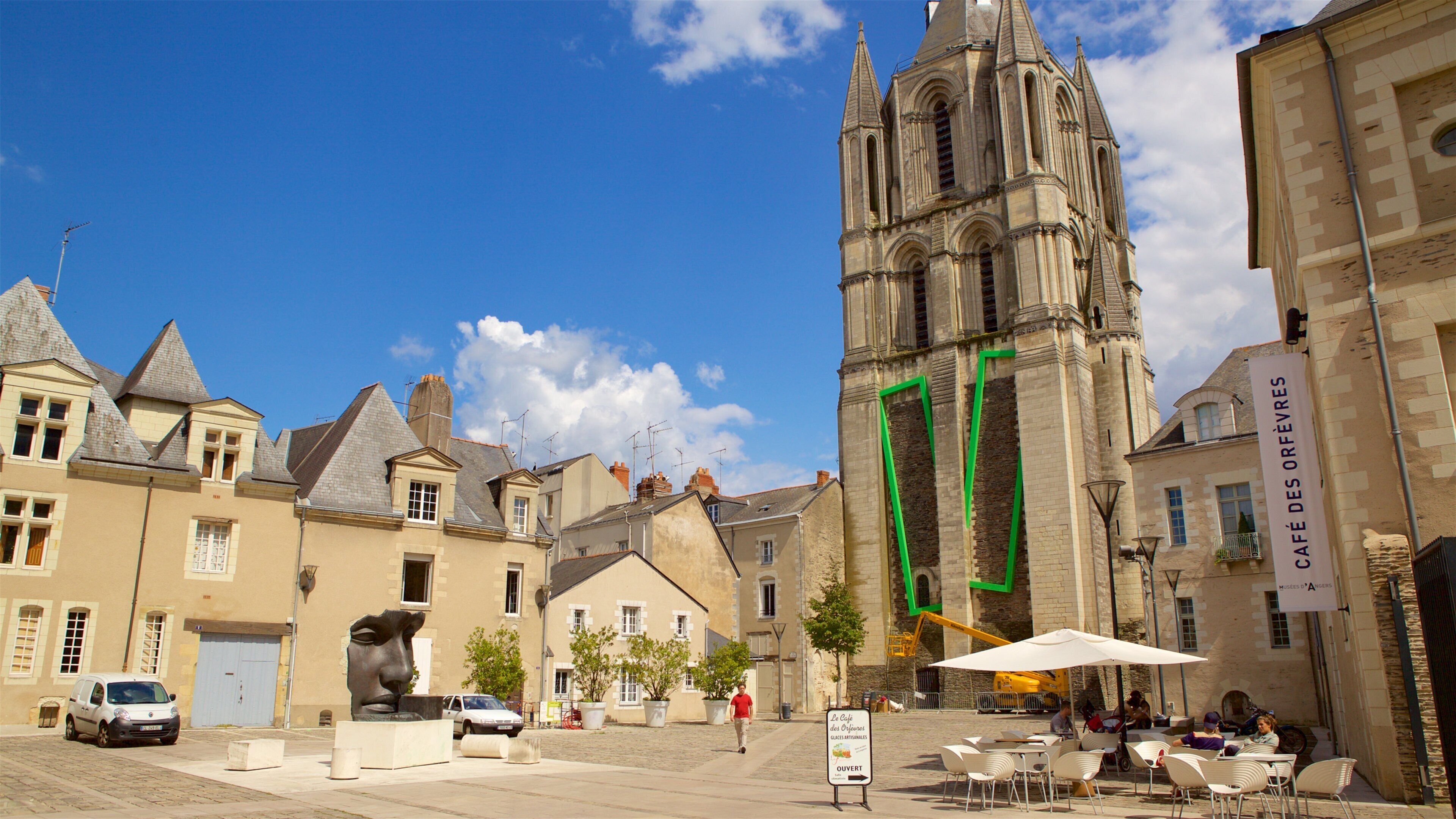 A historic church with a tall spire, a statue in the foreground, and outdoor seating at a café.
