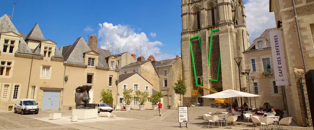 A historic church with a tall spire, a statue in the foreground, and outdoor seating at a café.