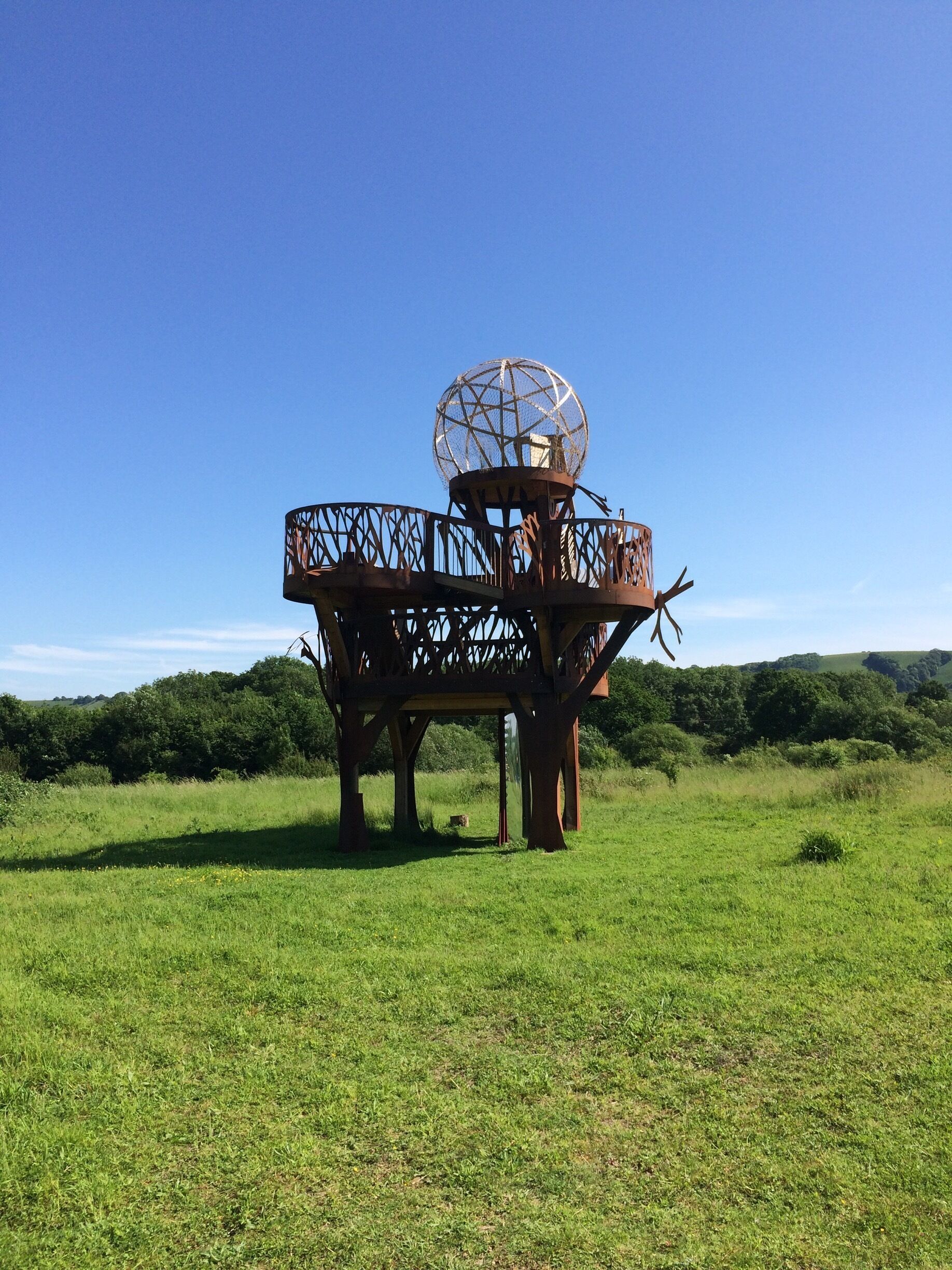 A metal structure with a spherical object on top, surrounded by a fence, in a grassy field.