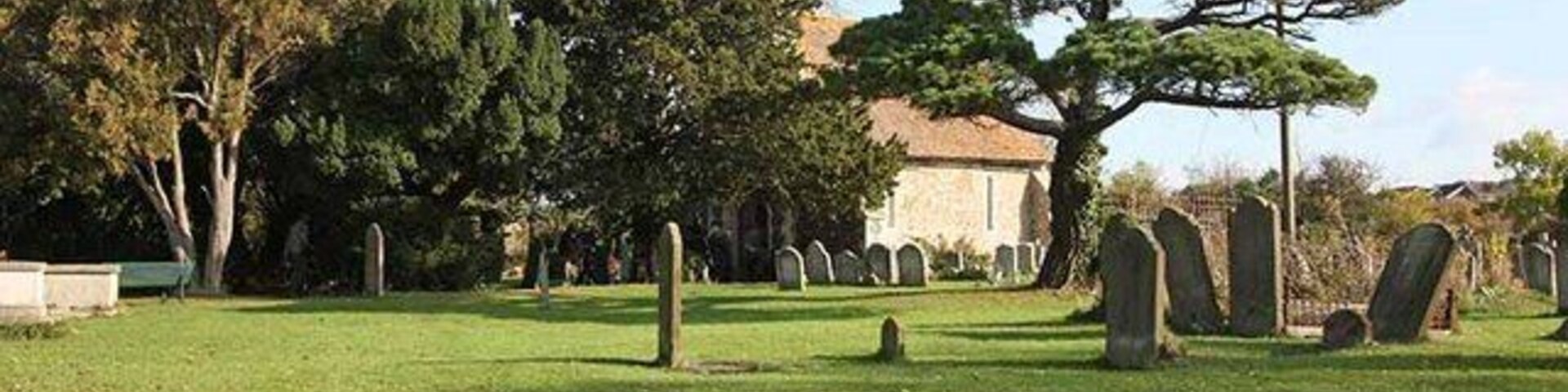 Um cemitério com lápides, árvores e um edifício ao fundo.