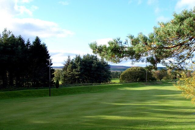 Un campo de golf con cielo despejado, césped verde y árboles.