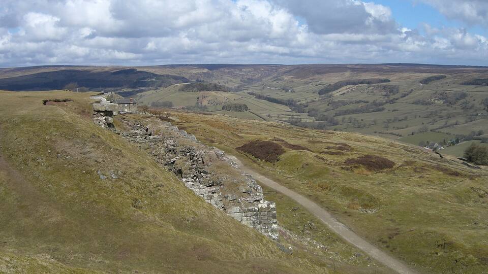A stone wall on a hillside with a path leading through a valley.