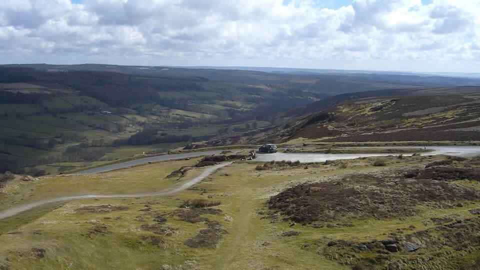 A valley with a winding road, a small body of water, and distant hills.