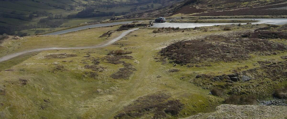A valley with a winding road, a small body of water, and distant hills.
