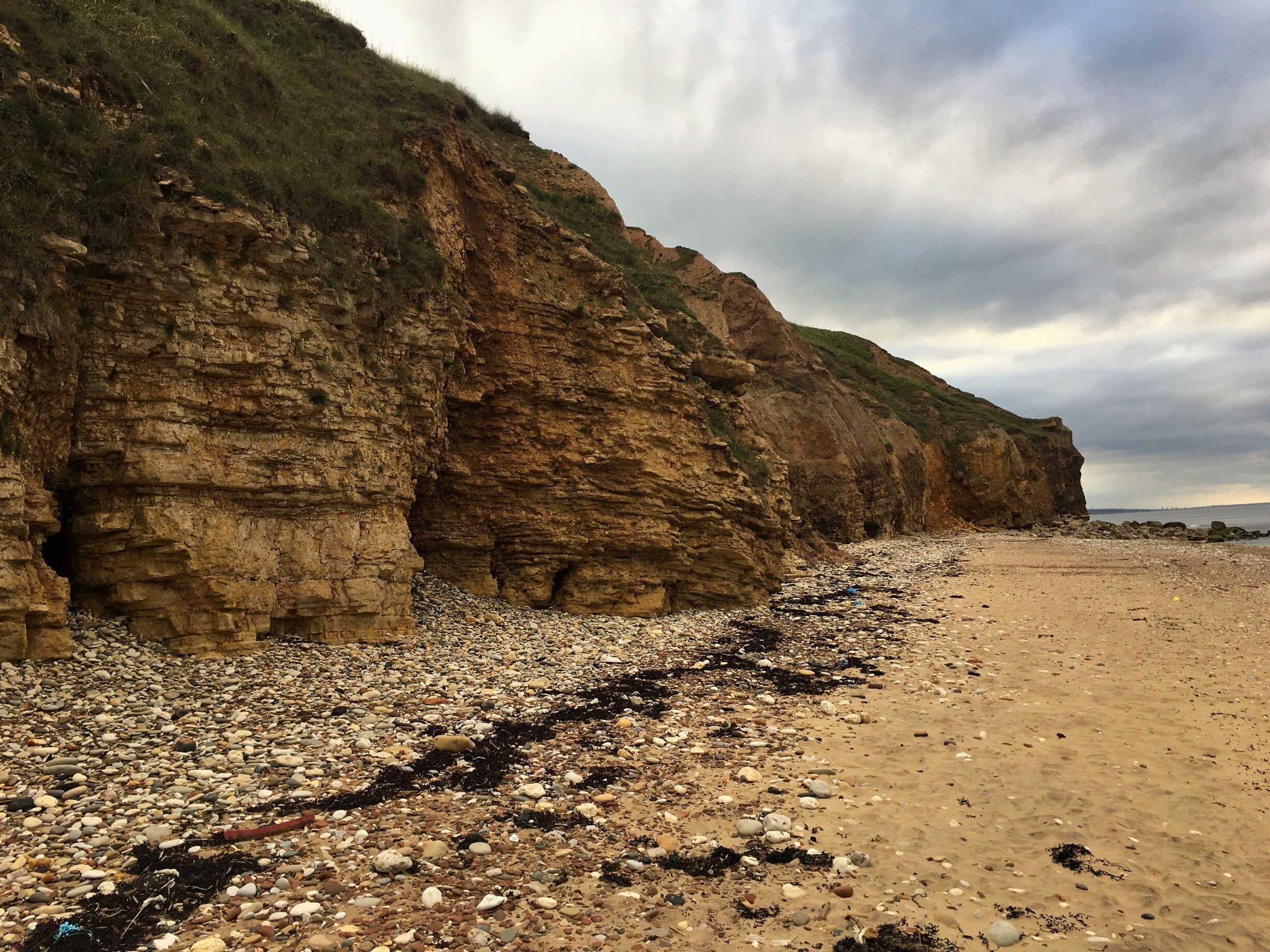 A rocky beach with layered cliffs and a cloudy sky.