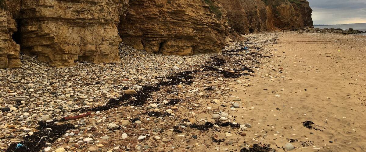 A rocky beach with layered cliffs and a cloudy sky.