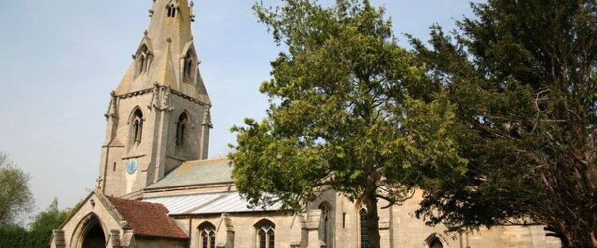 Una iglesia con una aguja alta y un árbol grande en primer plano.