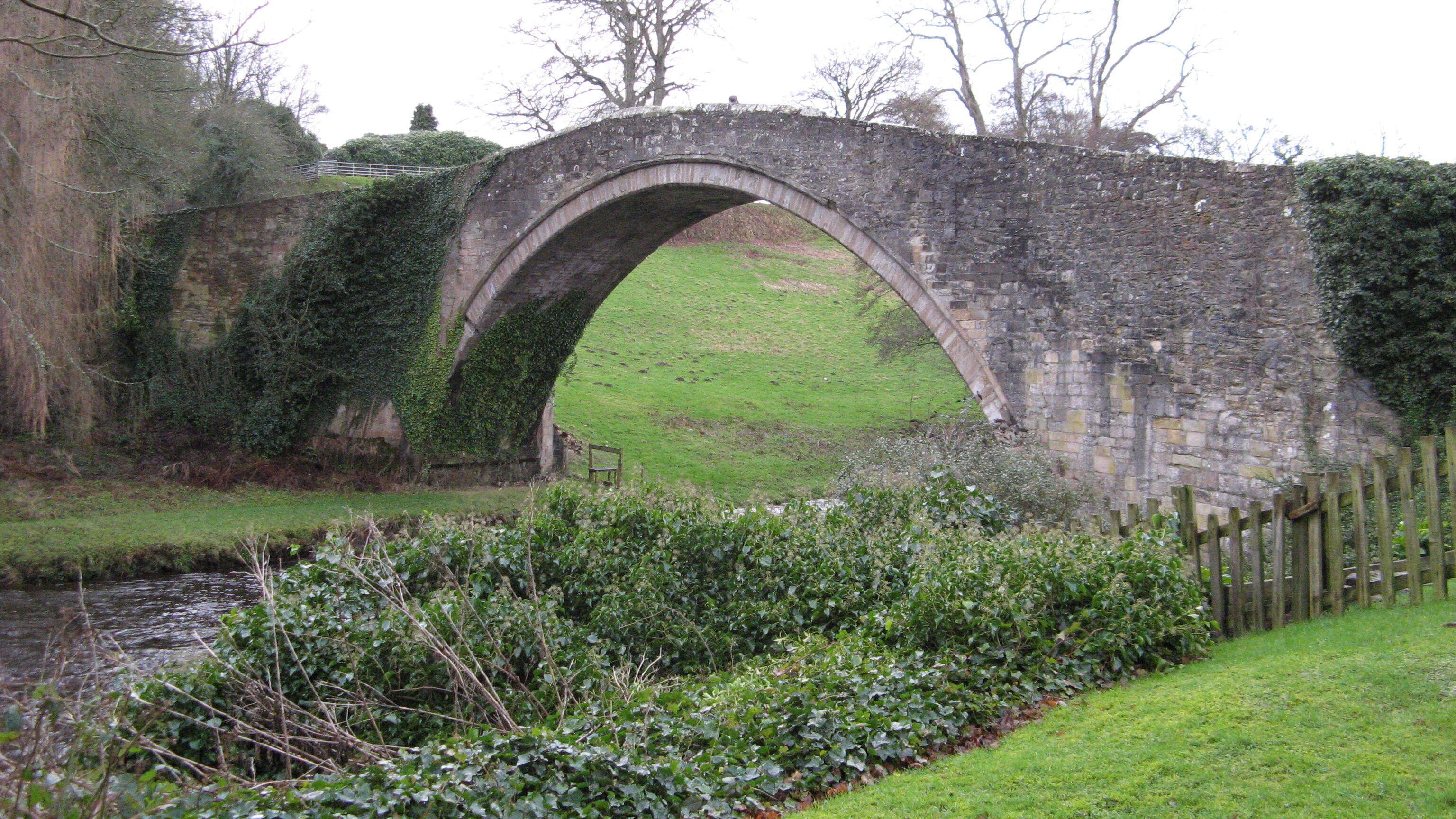 A stone bridge over a stream with greenery on either side.