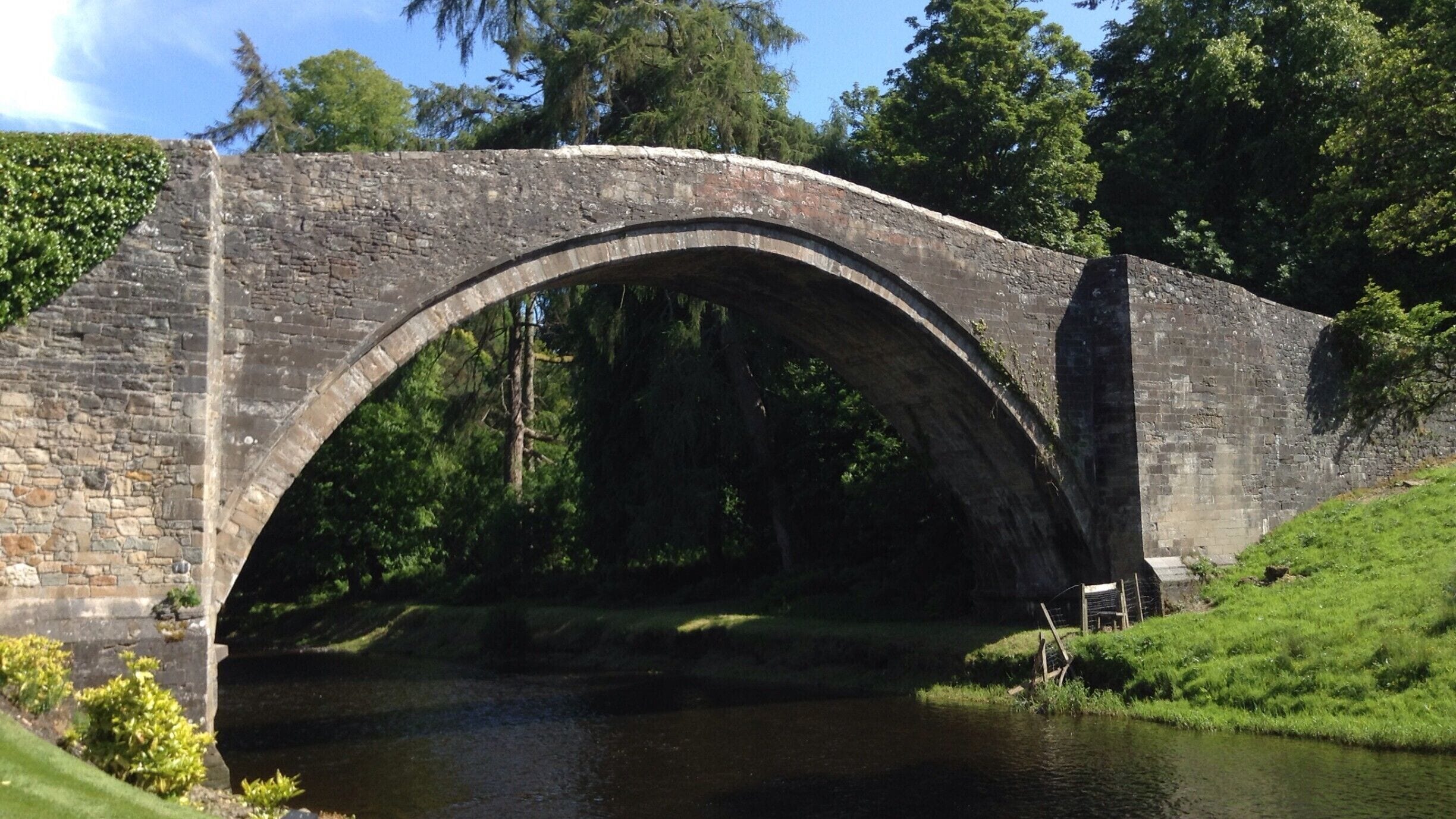 A stone bridge over a river with greenery and trees around.