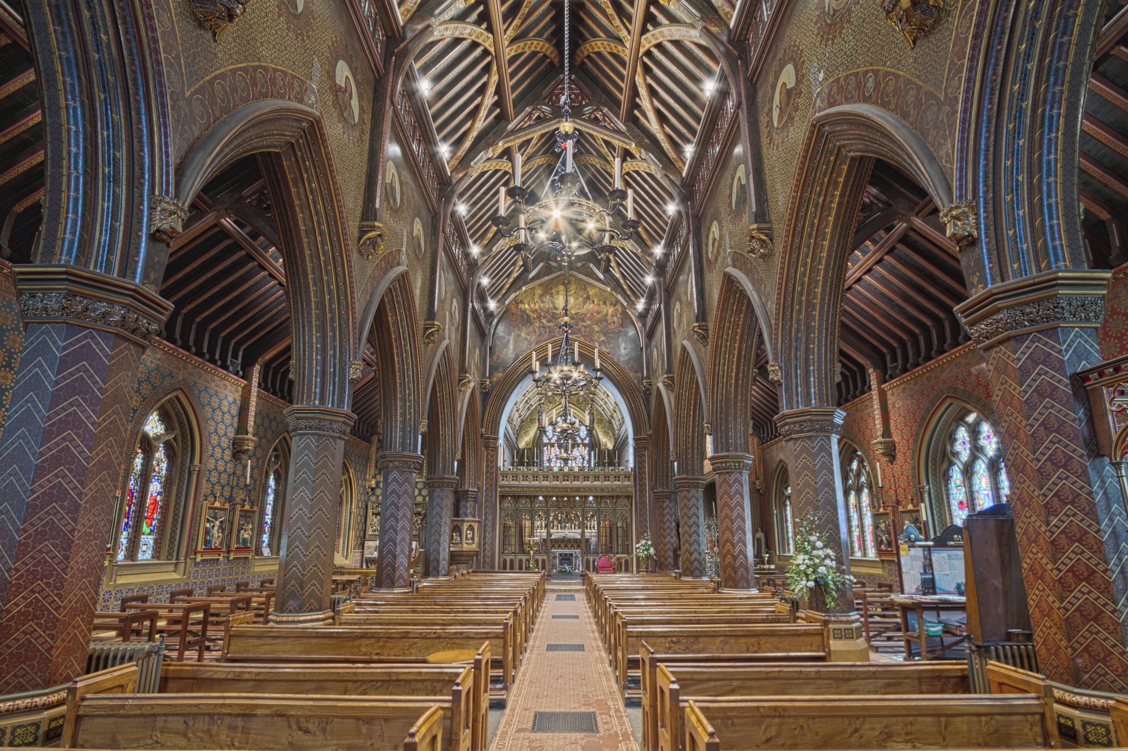 An ornate church interior with high vaulted ceilings, intricate woodwork, and a central altar.