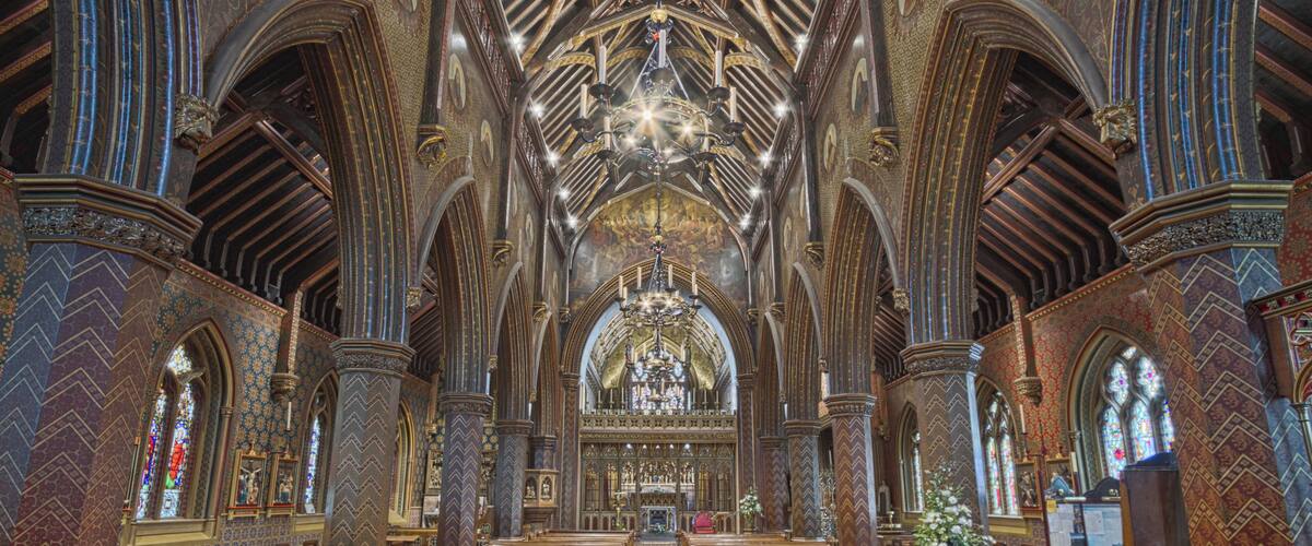 An ornate church interior with high vaulted ceilings, intricate woodwork, and a central altar.