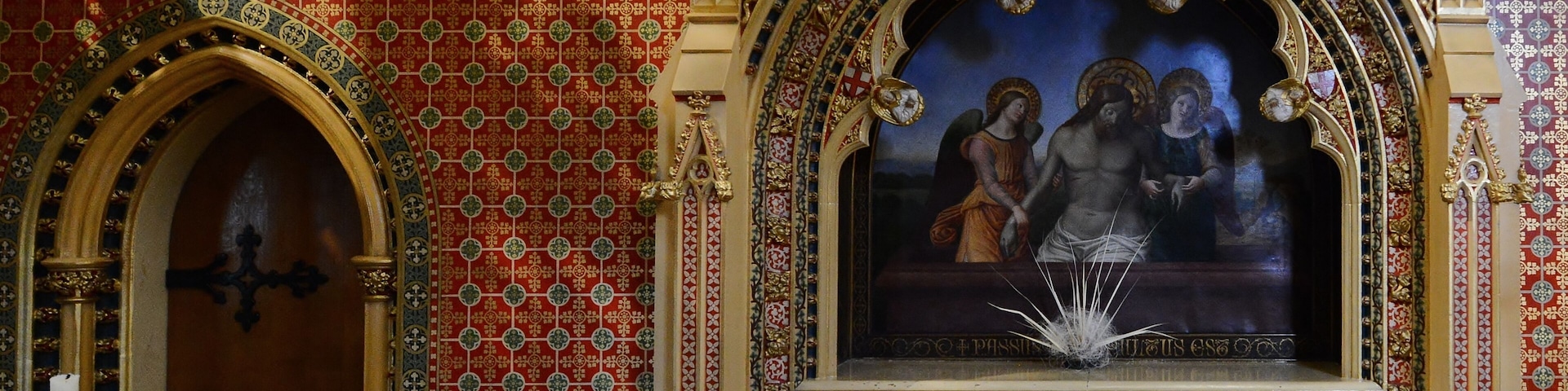 Interior de una iglesia ornamentada con un gran crucifijo, paredes con diseños y un techo detallado.