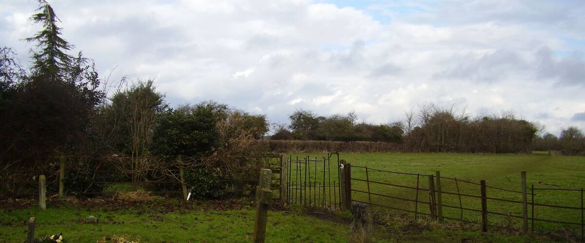 A rural landscape with a grassy field, a wooden fence, and a stone marker.