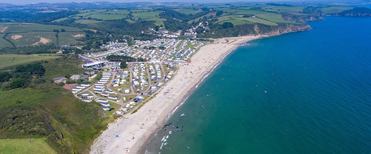 An aerial view of a coastal area with a beach, a row of caravans, and a clear blue sea.