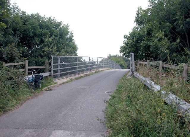 A rural road with a metal gate and a bicycle parked by the side.