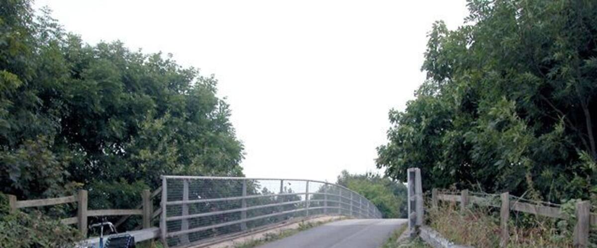A rural road with a metal gate and a bicycle parked by the side.