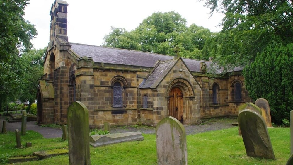 A historic stone church with a bell tower, surrounded by a cemetery with headstones.