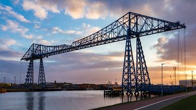 A large steel gantry bridge over a body of water with a sunset in the background.