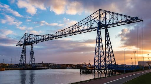 A large steel gantry bridge over a body of water with a sunset in the background.