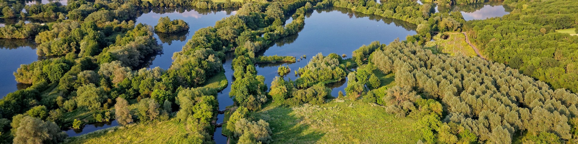 Um rio serpenteando por uma área arborizada com campos nas margens.