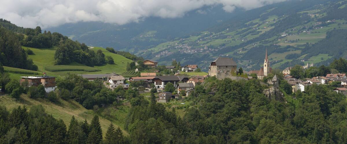 A village nestled in a valley with a church and castle, surrounded by lush green hills and clouds.