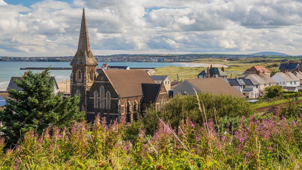 A coastal town with a prominent church tower, houses, and a beach.