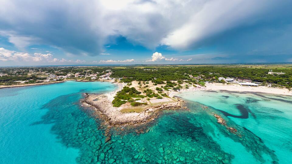A coastal town with clear turquoise waters, a sandy beach, and lush greenery.