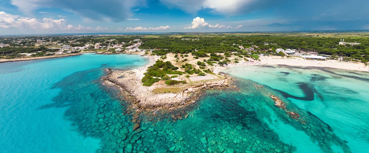 A coastal town with clear turquoise waters, a sandy beach, and lush greenery.