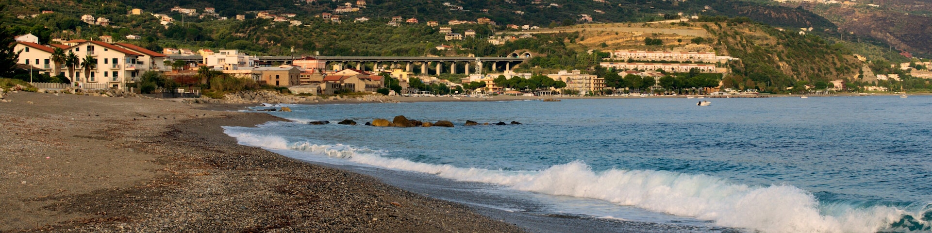 Picturesque autumn seascape the Tyrrhenian Sea near Patti, Sicily, Italy. Light waves and empty pebble beach. Cityscape in the background. Travel and tourism concept